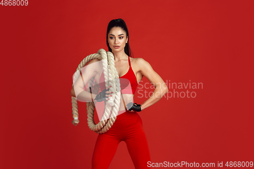 Image of Beautiful young female athlete practicing on red studio background, monochrome portrait