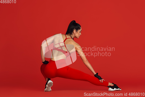 Image of Beautiful young female athlete practicing on red studio background, monochrome portrait