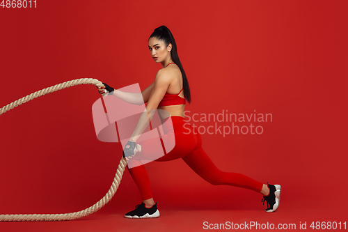 Image of Beautiful young female athlete practicing on red studio background, monochrome portrait