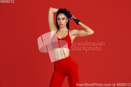 Image of Beautiful young female athlete practicing on red studio background, monochrome portrait