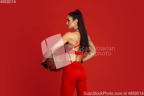 Image of Beautiful young female athlete practicing on red studio background, monochrome portrait