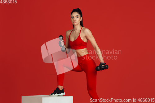 Image of Beautiful young female athlete practicing on red studio background, monochrome portrait