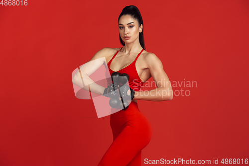 Image of Beautiful young female athlete practicing on red studio background, monochrome portrait