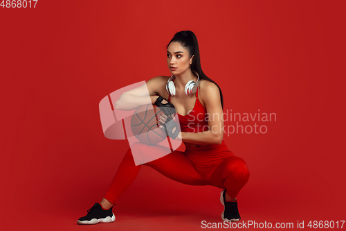 Image of Beautiful young female athlete practicing on red studio background, monochrome portrait