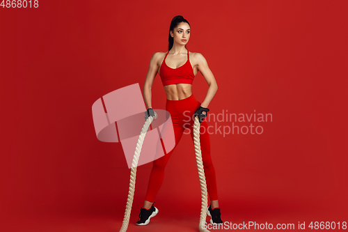 Image of Beautiful young female athlete practicing on red studio background, monochrome portrait