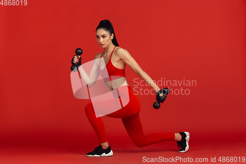 Image of Beautiful young female athlete practicing on red studio background, monochrome portrait