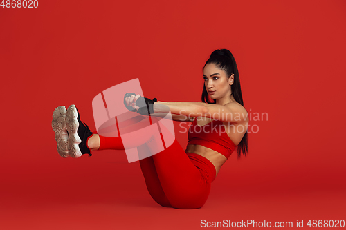 Image of Beautiful young female athlete practicing on red studio background, monochrome portrait