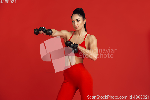 Image of Beautiful young female athlete practicing on red studio background, monochrome portrait