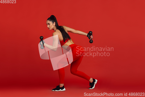 Image of Beautiful young female athlete practicing on red studio background, monochrome portrait