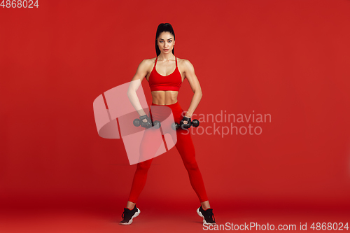 Image of Beautiful young female athlete practicing on red studio background, monochrome portrait