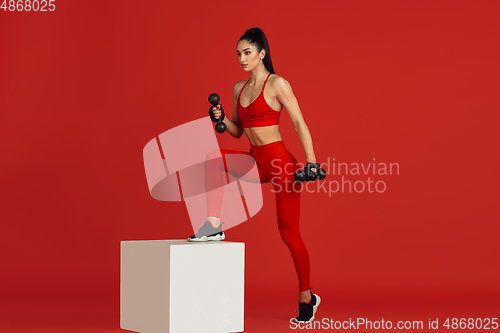 Image of Beautiful young female athlete practicing on red studio background, monochrome portrait