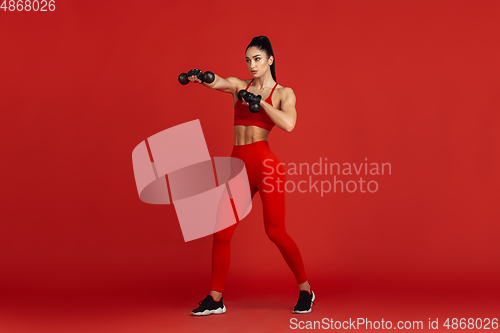 Image of Beautiful young female athlete practicing on red studio background, monochrome portrait