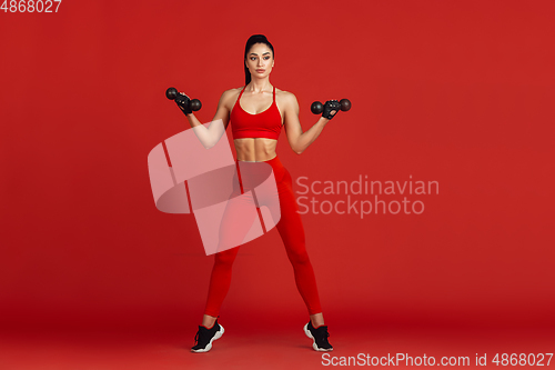 Image of Beautiful young female athlete practicing on red studio background, monochrome portrait