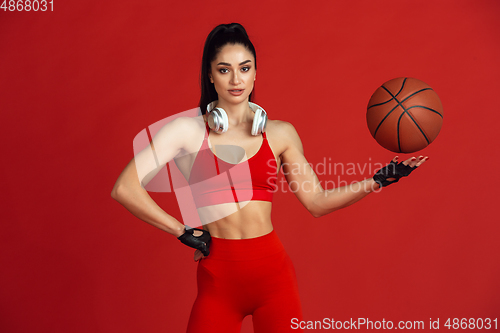 Image of Beautiful young female athlete practicing on red studio background, monochrome portrait