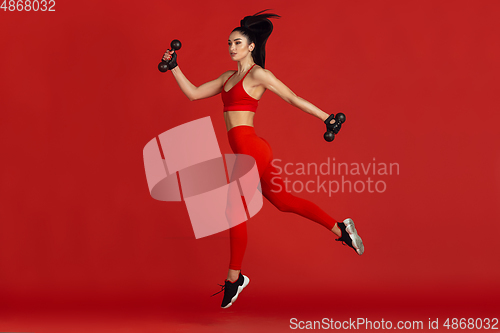 Image of Beautiful young female athlete practicing on red studio background, monochrome portrait