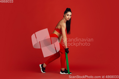 Image of Beautiful young female athlete practicing on red studio background, monochrome portrait