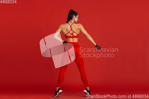 Image of Beautiful young female athlete practicing on red studio background, monochrome portrait