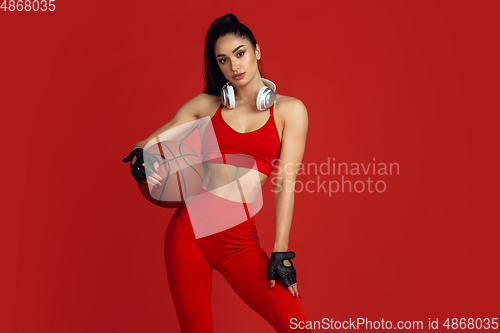 Image of Beautiful young female athlete practicing on red studio background, monochrome portrait