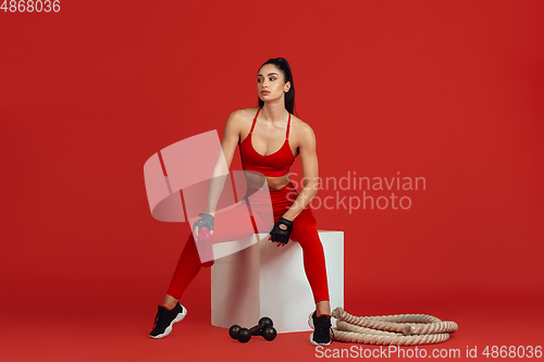 Image of Beautiful young female athlete practicing on red studio background, monochrome portrait