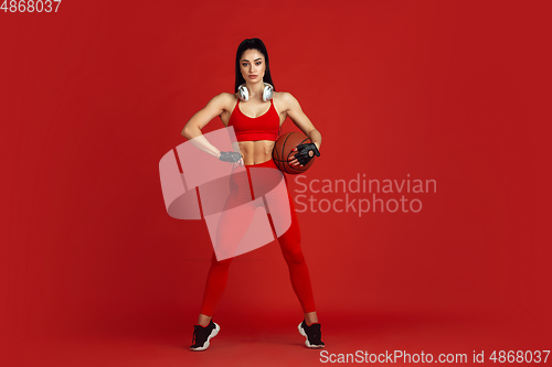 Image of Beautiful young female athlete practicing on red studio background, monochrome portrait