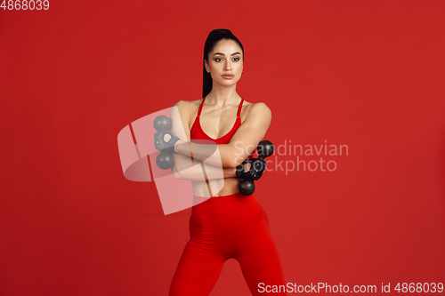 Image of Beautiful young female athlete practicing on red studio background, monochrome portrait