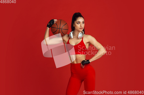 Image of Beautiful young female athlete practicing on red studio background, monochrome portrait