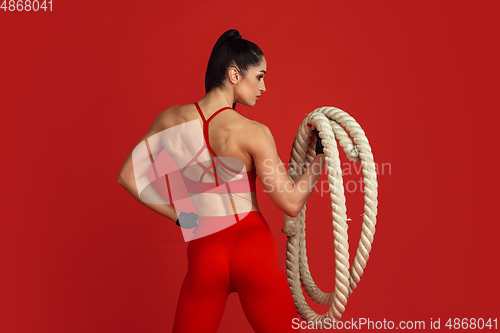 Image of Beautiful young female athlete practicing on red studio background, monochrome portrait