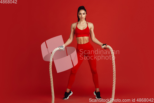 Image of Beautiful young female athlete practicing on red studio background, monochrome portrait