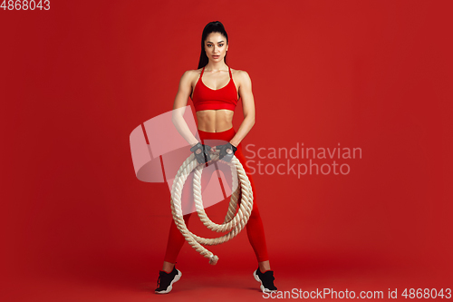 Image of Beautiful young female athlete practicing on red studio background, monochrome portrait