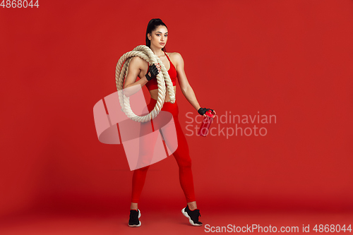 Image of Beautiful young female athlete practicing on red studio background, monochrome portrait