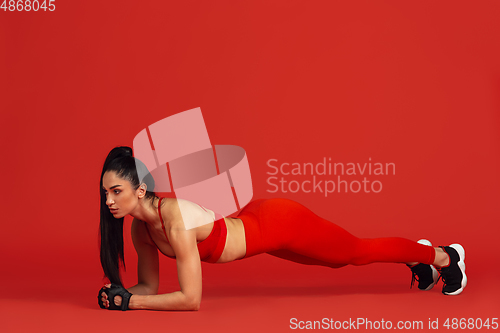 Image of Beautiful young female athlete practicing on red studio background, monochrome portrait