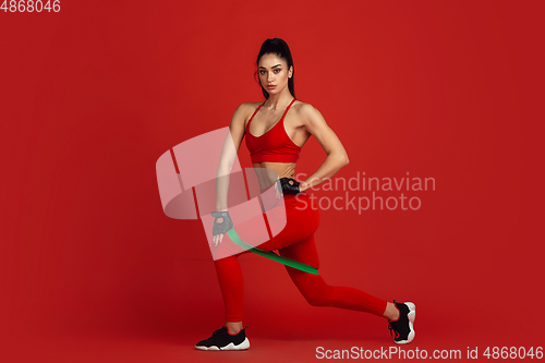 Image of Beautiful young female athlete practicing on red studio background, monochrome portrait