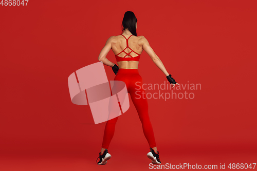 Image of Beautiful young female athlete practicing on red studio background, monochrome portrait