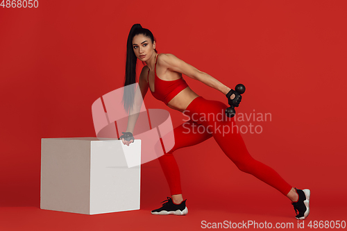 Image of Beautiful young female athlete practicing on red studio background, monochrome portrait