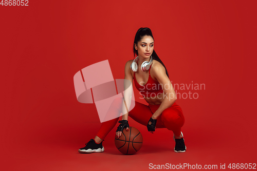 Image of Beautiful young female athlete practicing on red studio background, monochrome portrait