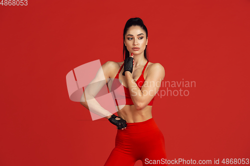 Image of Beautiful young female athlete practicing on red studio background, monochrome portrait