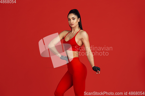 Image of Beautiful young female athlete practicing on red studio background, monochrome portrait