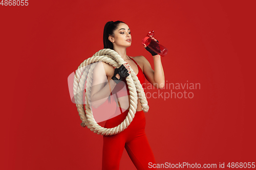 Image of Beautiful young female athlete practicing on red studio background, monochrome portrait