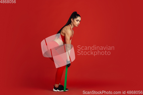 Image of Beautiful young female athlete practicing on red studio background, monochrome portrait