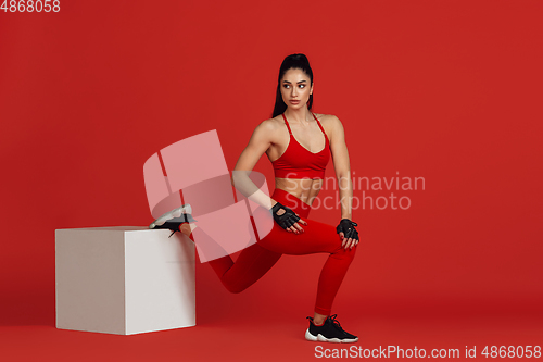 Image of Beautiful young female athlete practicing on red studio background, monochrome portrait