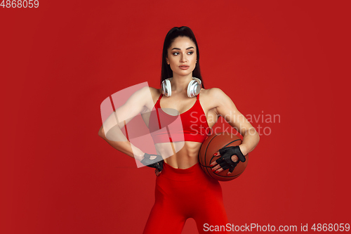 Image of Beautiful young female athlete practicing on red studio background, monochrome portrait