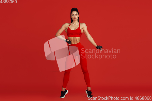 Image of Beautiful young female athlete practicing on red studio background, monochrome portrait