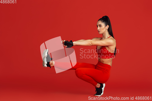 Image of Beautiful young female athlete practicing on red studio background, monochrome portrait