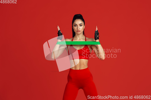 Image of Beautiful young female athlete practicing on red studio background, monochrome portrait