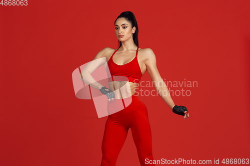 Image of Beautiful young female athlete practicing on red studio background, monochrome portrait