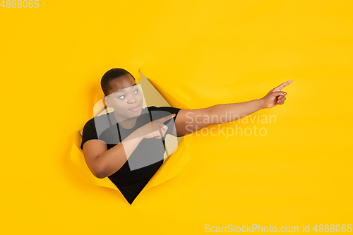 Image of Cheerful young woman poses in torn yellow paper hole background, emotional and expressive