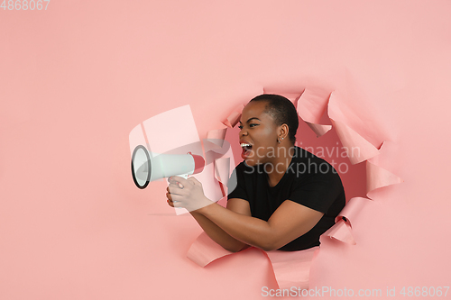 Image of Cheerful young woman poses in torn coral paper hole background, emotional and expressive, shouting with speaker
