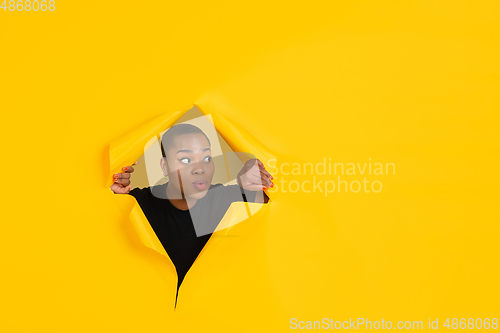 Image of Cheerful young woman poses in torn yellow paper hole background, emotional and expressive