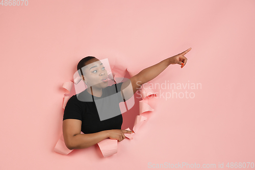 Image of Cheerful young woman poses in torn coral paper hole background, emotional and expressive