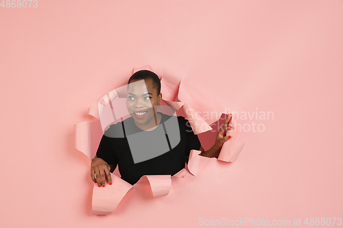 Image of Cheerful young woman poses in torn coral paper hole background, emotional and expressive